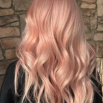 Person with long, wavy, pastel pink hair facing a stone wall background.